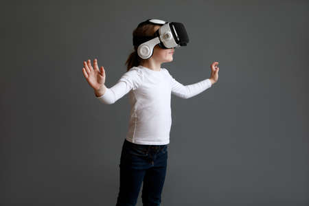Little girl wearing VR goggles holding out her arms in delight against gray background.の写真素材