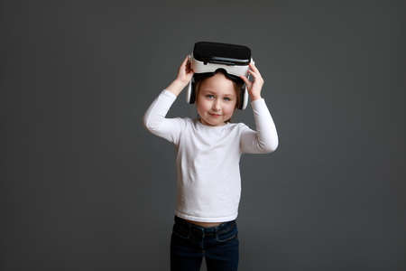 Portrait of female child in white long sleeve shirt wearing virtual reality glasses over gray background.の写真素材
