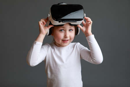 Smiling little kid girl in white long sleeve shirt isolated on gray background wearing VR glasses.の写真素材