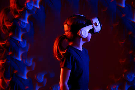 Kid girl experiencing VR headset game on colorful background with effect reflections. Child using a gaming gadget for virtual reality. Futuristic goggles at young age. Virtual technology.の写真素材