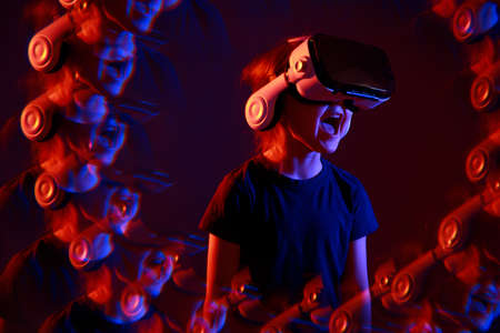 Kid girl experiencing VR headset game on colorful background with effect reflections. Child using a gaming gadget for virtual reality. Futuristic goggles at young age. Virtual technology.の写真素材