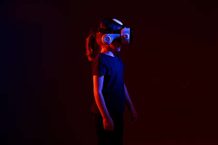 Girl 5 yo experiencing VR headset game on colorful background. Child using a gaming gadget for virtual reality. Futuristic goggles at young age. Virtual technology.の写真素材