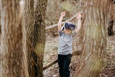 Happy kid playing and watching visual reality glasses or VR technology on forest beautiful nature.の写真素材