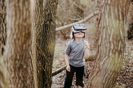 Happy kid playing and watching visual reality glasses or VR technology on forest beautiful nature.の写真素材