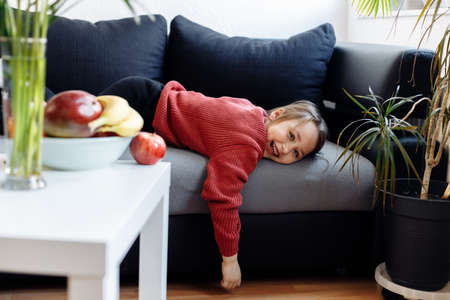 Healthy lifestyle concept - child lying on sofa, lots of fresh fruit on the table in front at home.の写真素材