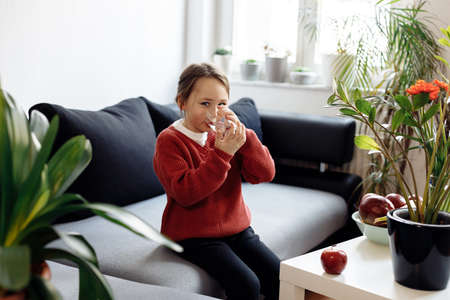 Healthy eating - child holding and drinking glass of water, lots of fresh fruit on the table in front at home, healthy lifestyle conceptの写真素材