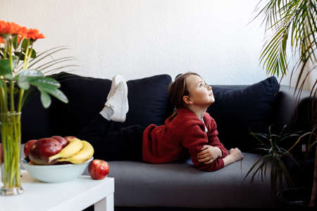 Healthy lifestyle concept - little child lying on sofa, lots of fresh fruit on the table in front at home.の写真素材