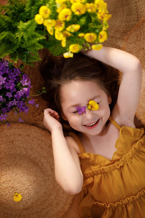 Portrait of a little girl with flowers on face lying on background from straw hats, summer and travel feeling concept.の写真素材