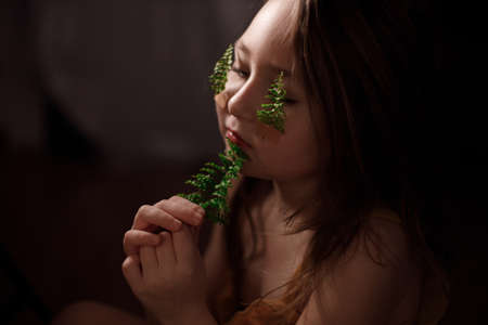 Ecology concept, portrait of little girl with fern sprigs pasted with plasters on her cheeks.の写真素材