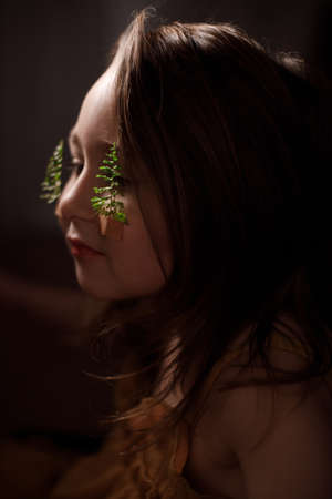 Ecology concept, portrait of little girl with fern sprigs pasted with plasters on her cheeks.