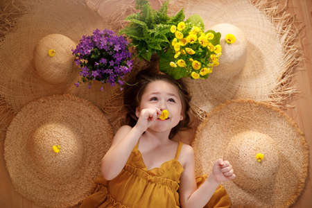 Portrait of a little girl lying on background with flowers and straw hat, summer and travel feeling concept.の写真素材