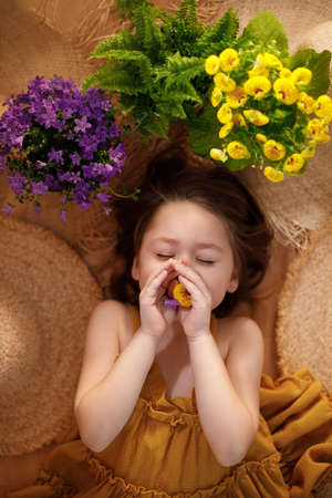 Portrait of a little girl lying on background with flowers and straw hat, summer and travel feeling concept.の写真素材