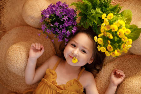 Portrait of a little girl lying on background with flowers and straw hat, summer and travel feeling concept.の写真素材