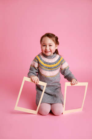 Portrait of a little smiling girl holding blank frame for mock-up on a pink background.の写真素材