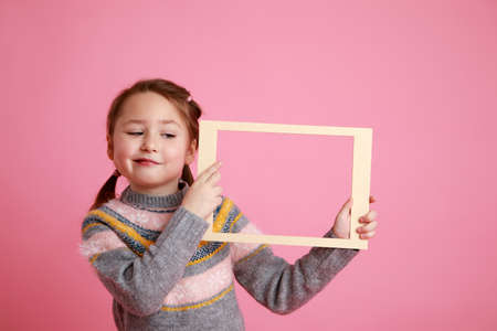 Portrait of a little smiling girl holding blank frame for mock-up on a pink background.の写真素材