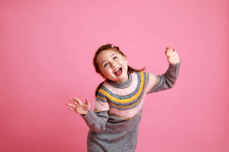 Studio portrait of funny smiling preschool girl in warm dress on pink background laughing and screaming.の写真素材
