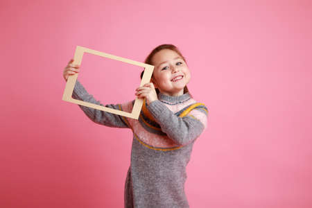 Portrait of a little smiling girl holding blank frame for mock-up on a pink background.の写真素材