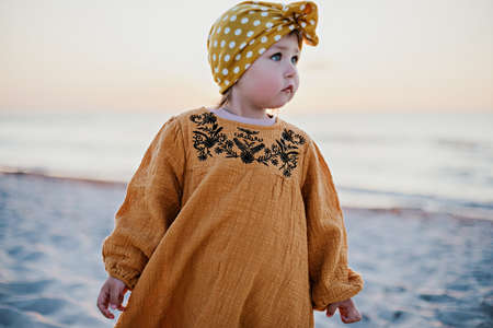Little girl in oriental clothes walking along the beach at sunsetの写真素材