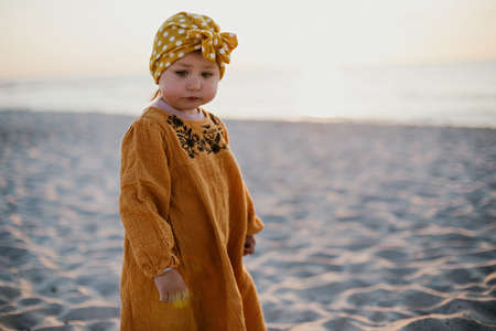 Little girl in oriental clothes walking along the beach at sunsetの写真素材