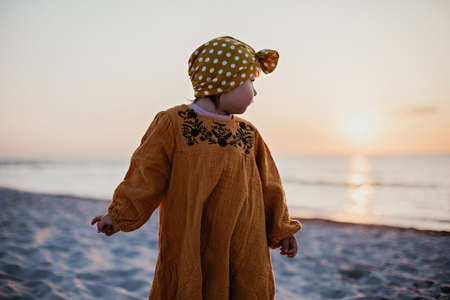 Little girl in oriental clothes walking along the beach at sunsetの写真素材