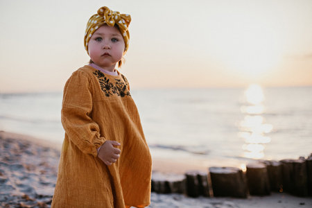 Little girl in oriental clothes walking along the beach at sunsetの写真素材