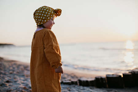 Little girl in oriental clothes walking along the beach at sunsetの写真素材