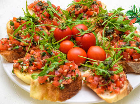 Tasty savory tomato Italian appetizers, or bruschetta, on slices of toasted baguette garnished with pesto and ruccolaの写真素材