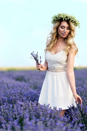 Beautiful Girl in lavender Field. Pretty woman Provence style in white dress and flowers wreath. Beautiful blonde woman in the lavender field on sunset Amazing portraitの写真素材