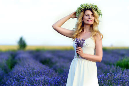 Beautiful Girl in lavender Field. Pretty woman Provence style in white dress and flowers wreath. Beautiful blonde woman in the lavender field on sunset Amazing portraitの写真素材