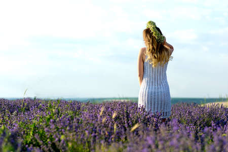 Beautiful Girl in lavender Field. Pretty woman Provence style in white dress and flowers wreath. Beautiful blonde woman in the lavender field on sunset Amazing portraitの写真素材