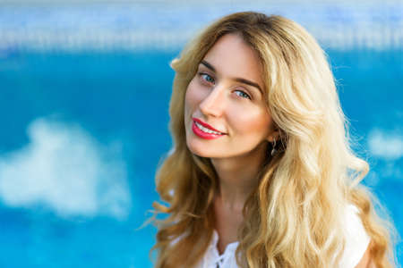 Happy young woman smiling. Curly blonde hair and red lips. Blue Backgroundの写真素材