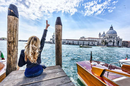 Blonde girl sitting on the pier in Venice. Back viewの写真素材
