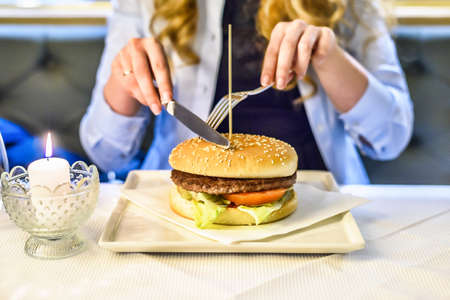 Woman eating a burger in a restaurant. knife and fork