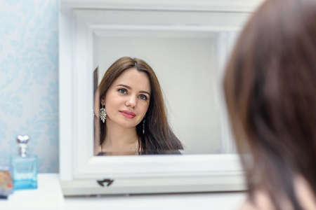 Brunette girl looking in the mirror portrait. Modern looksの写真素材