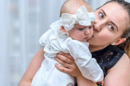 Mother kissing her baby girl. Cute toddler dressed in whites