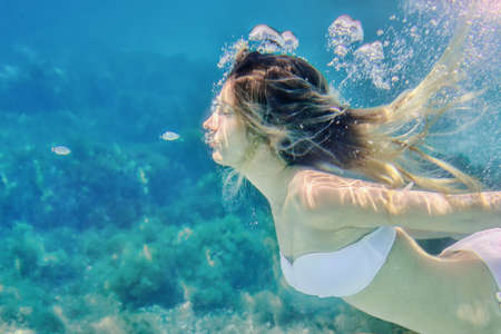 Girl and small fishes swimming underwater portrait. Sea summer blue water background with bubblesの写真素材
