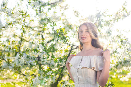 Woman in a blooming orchard at springtime. Enjoying sunny warm day. Retro style dress. Colorful...