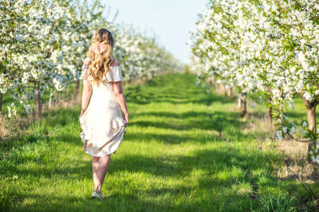 Woman in a blooming orchard at springtime. Enjoying sunny warm day. Retro style dress. Colorful spring moodsの写真素材