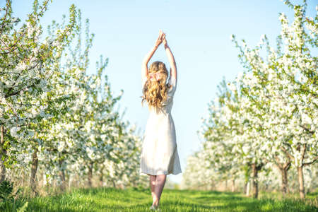Woman in a blooming orchard at springtime. Enjoying sunny warm day. Retro style dress. Colorful spring moodsの写真素材