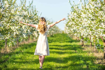 Woman in a blooming orchard at springtime. Enjoying sunny warm day. Retro style dress. Colorful spring moodsの写真素材