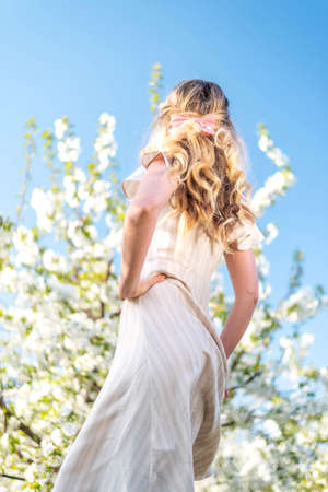 Woman in a blooming orchard at springtime. Enjoying sunny warm day. Retro style dress. Colorful spring moodsの写真素材