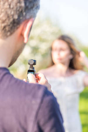 Man filming with a modern video camera in the park. Spring time shooting ideas. Behind the scenes shooting vlogsの写真素材