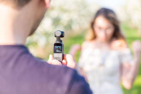 Man filming with a modern video camera in an orchard. Spring time shooting ideas. Behind the scenes shooting vlogsの写真素材