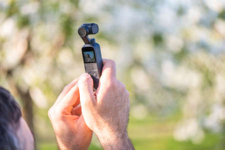 Man hands holding a tiny modern video camera in a park. Spring time filming ideasの写真素材