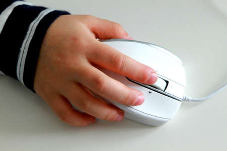 Child holding computer mouse on white tableの写真素材