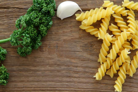 Raw Fussilli Pasta with garlic and parsley on wooden table with space for your messageの写真素材