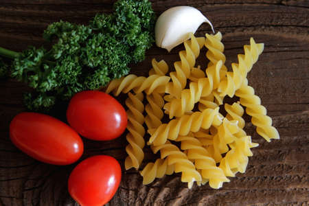 Raw fussilli pasta with tomatoes, garlic and parsley on wooden tableの写真素材