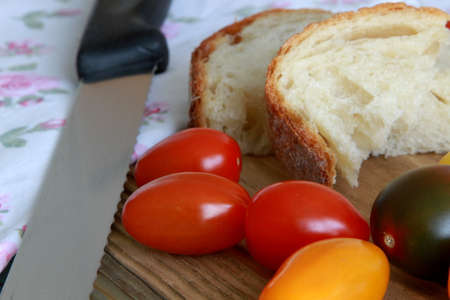 Bread slices with colorful tomatoes, kitchen towel and knife on wooden tableの写真素材