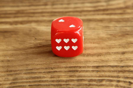 Red dice / cube with hearts on wooden background
