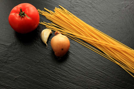 Raw spaghetti, onion and garlic on black backgroundの写真素材